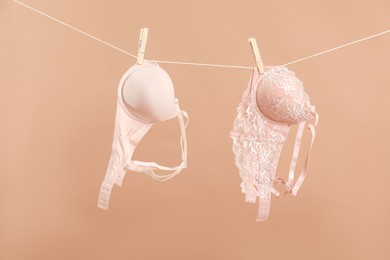 Photo of Beautiful bras hanging on rope against dark beige background