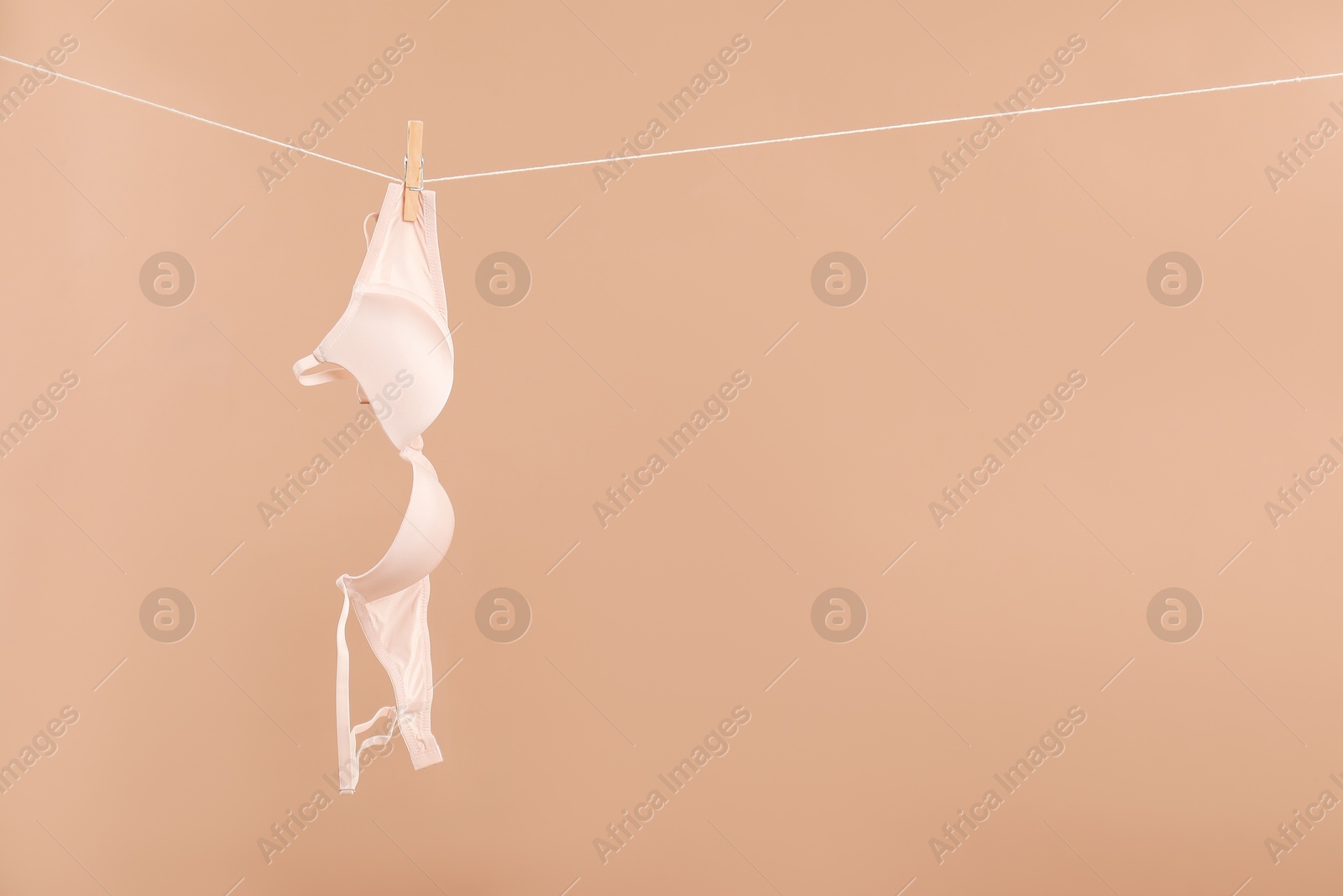 Photo of Beautiful bra hanging on rope against dark beige background, space for text