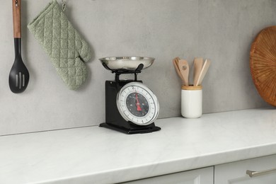 Photo of Retro mechanical kitchen scale on white marble countertop and other utensils indoors