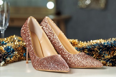 Elegant high heeled shoes and tinsel on white wooden table indoors, closeup