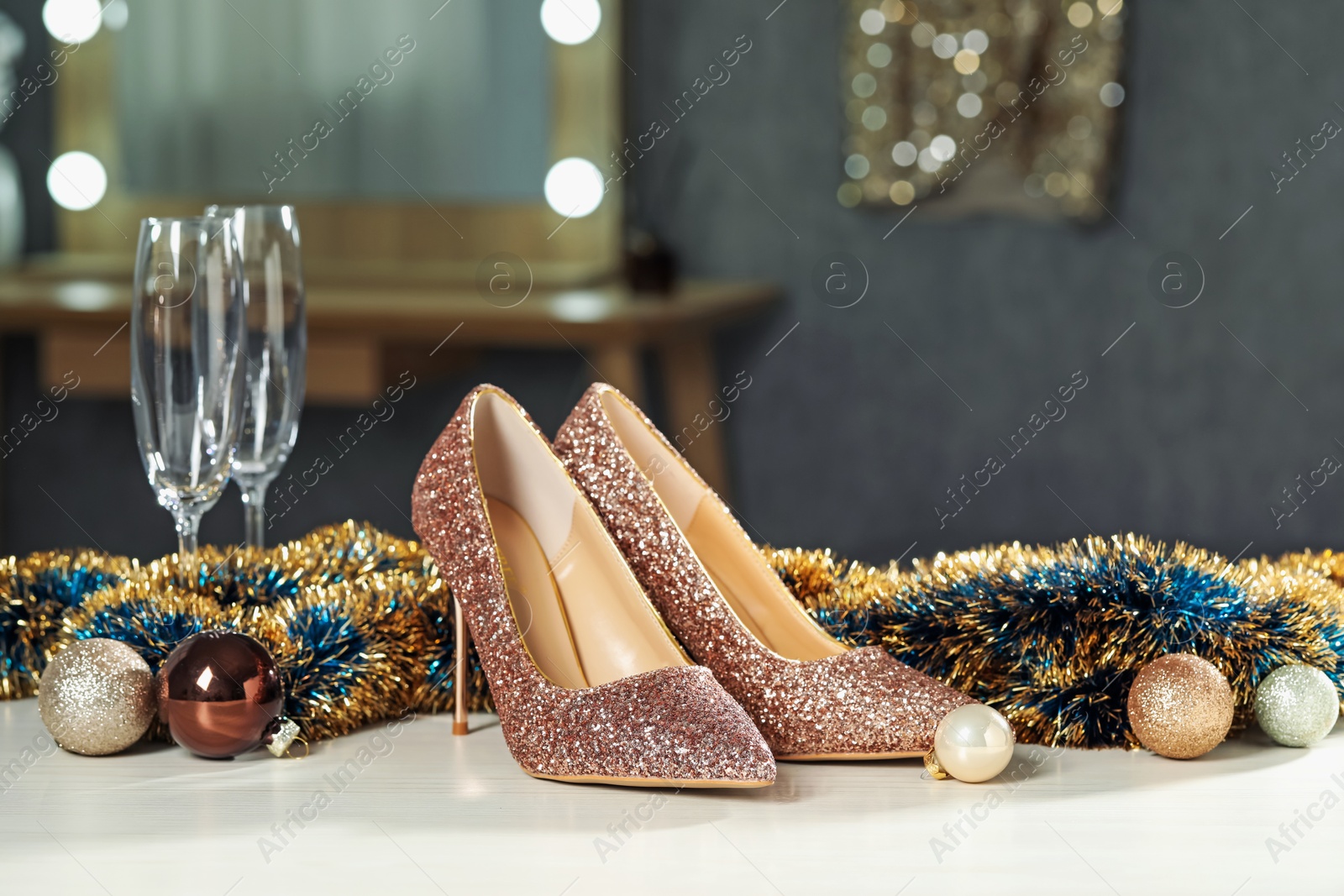 Photo of Elegant high heeled shoes, tinsel, baubles and glasses on white table indoors