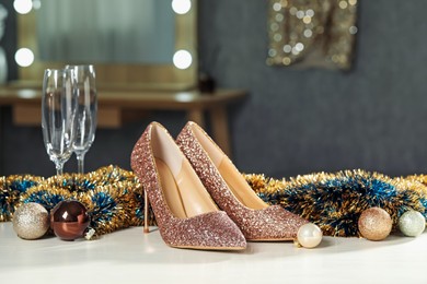 Photo of Elegant high heeled shoes, tinsel, baubles and glasses on white table indoors