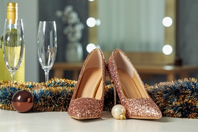 Elegant high heeled shoes, tinsel, baubles, bottle and glasses on white table indoors