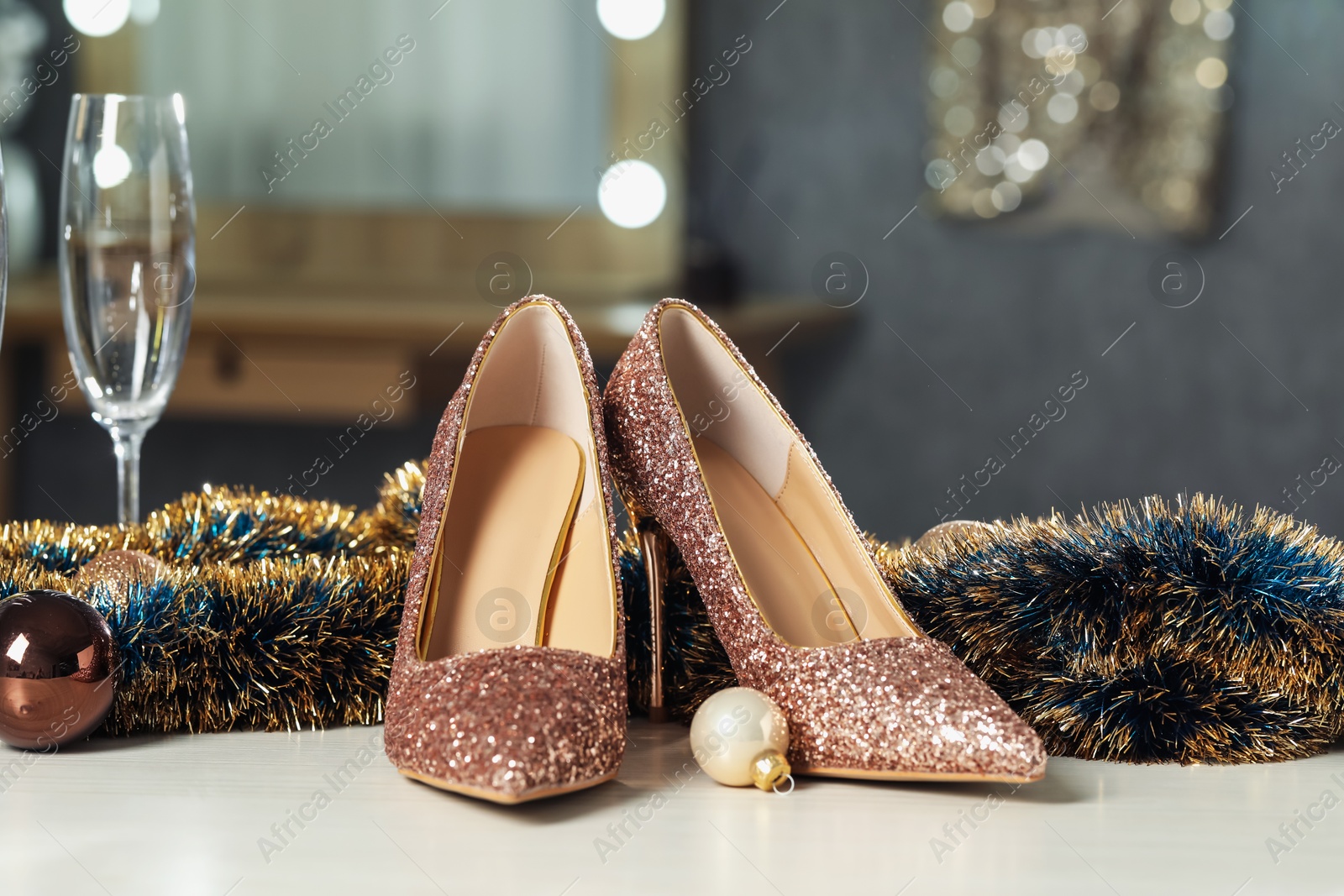 Photo of Elegant high heeled shoes, tinsel, baubles and glass on white table indoors