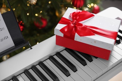 Photo of Synthesizer with gift box near Christmas tree indoors, closeup