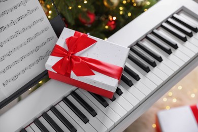 Photo of Synthesizer with music sheet and gift box near Christmas tree indoors, above view