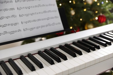 Photo of Synthesizer with music sheets against blurred Christmas lights, closeup. Bokeh effect