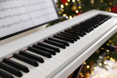 Photo of Synthesizer with music sheets against blurred Christmas lights, closeup. Bokeh effect