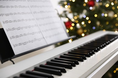 Photo of Synthesizer with music sheets against blurred Christmas lights, closeup. Bokeh effect