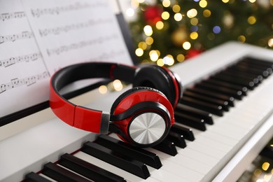 Photo of Synthesizer with music sheets and headphones against blurred Christmas lights, closeup. Bokeh effect