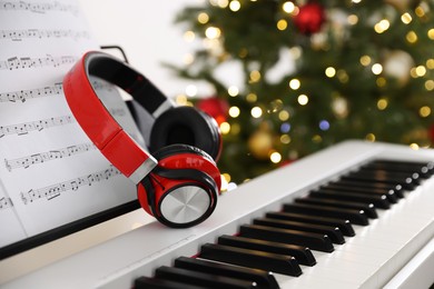 Photo of Synthesizer with music sheets and headphones against blurred Christmas lights, closeup. Bokeh effect