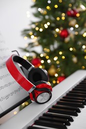 Photo of Synthesizer with music sheets and headphones against blurred Christmas lights, closeup. Bokeh effect