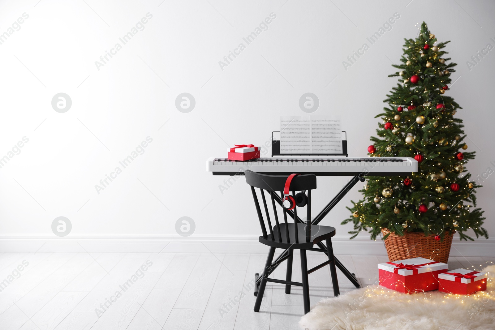 Synthesizer with music sheets and gift boxes near Christmas tree indoors, space for text Photo of Synthesizer with music sheets and gift boxes near Christmas tree indoors, space for text