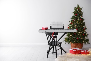 Photo of Synthesizer with music sheets and gift boxes near Christmas tree indoors, space for text