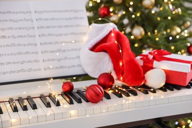 Photo of Synthesizer with music sheets and Christmas decor against blurred festive lights, closeup