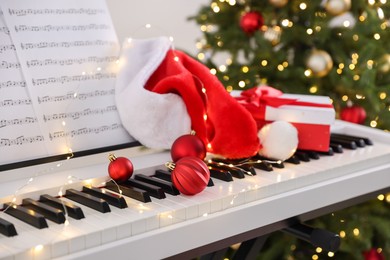 Photo of Synthesizer with music sheets and Christmas decor against blurred festive lights, closeup