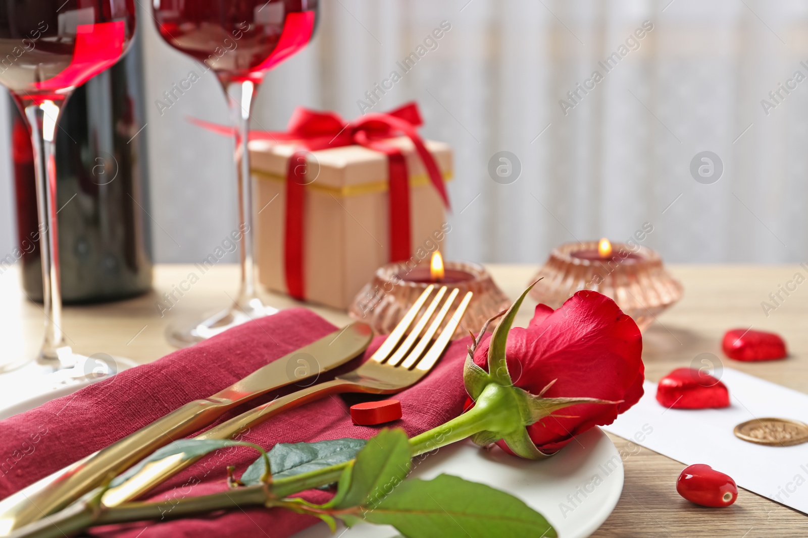 Photo of Romantic place setting with red rose on table, closeup. Valentine's day celebration