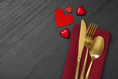 Romantic place setting with red hearts and cutlery on black table, top view. Valentine's day celebration