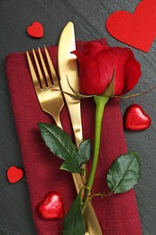 Romantic place setting with red rose and cutlery on black table, top view. Valentine's day celebration