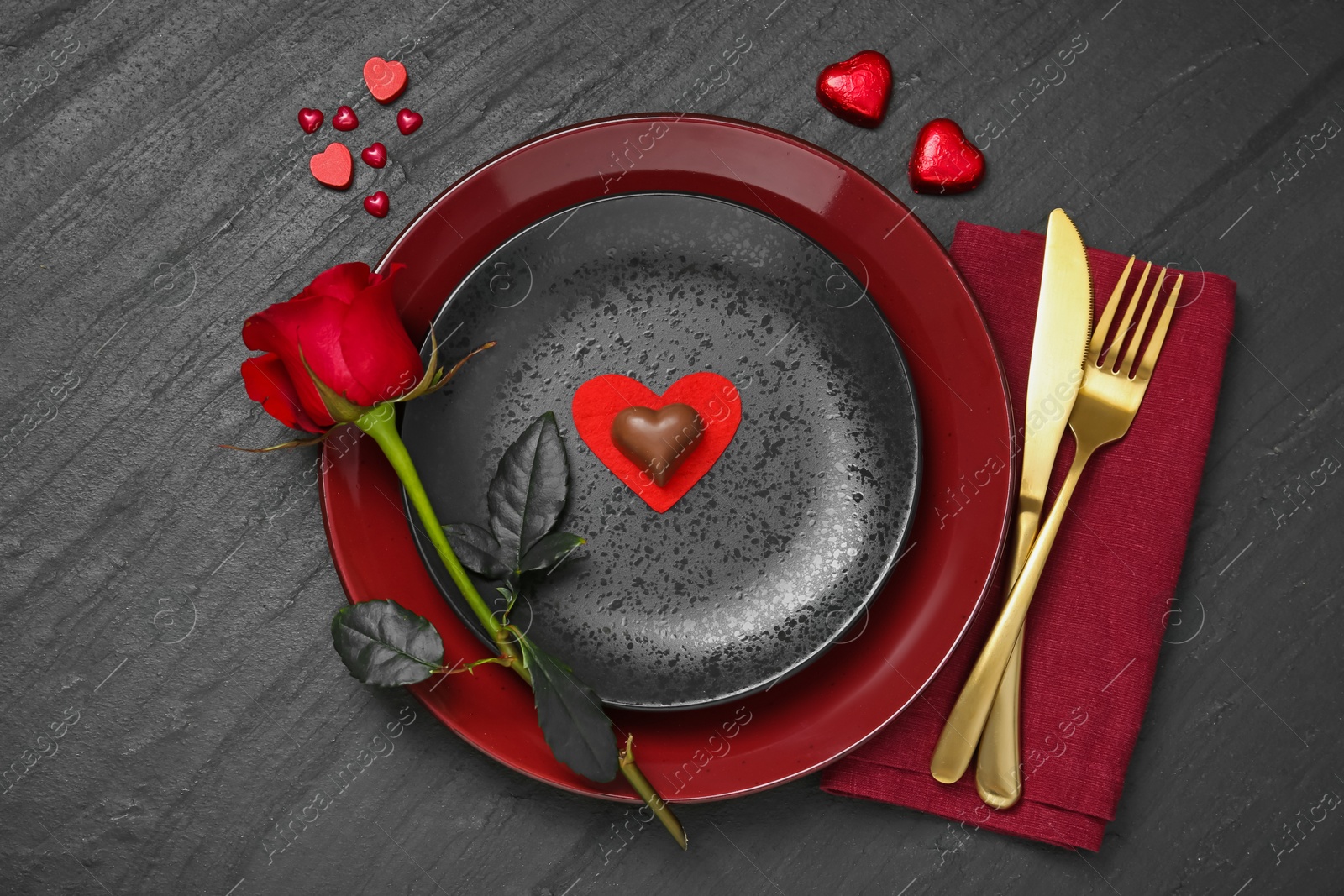 Photo of Romantic place setting with rose and plates on black table, top view. Valentine's day celebration