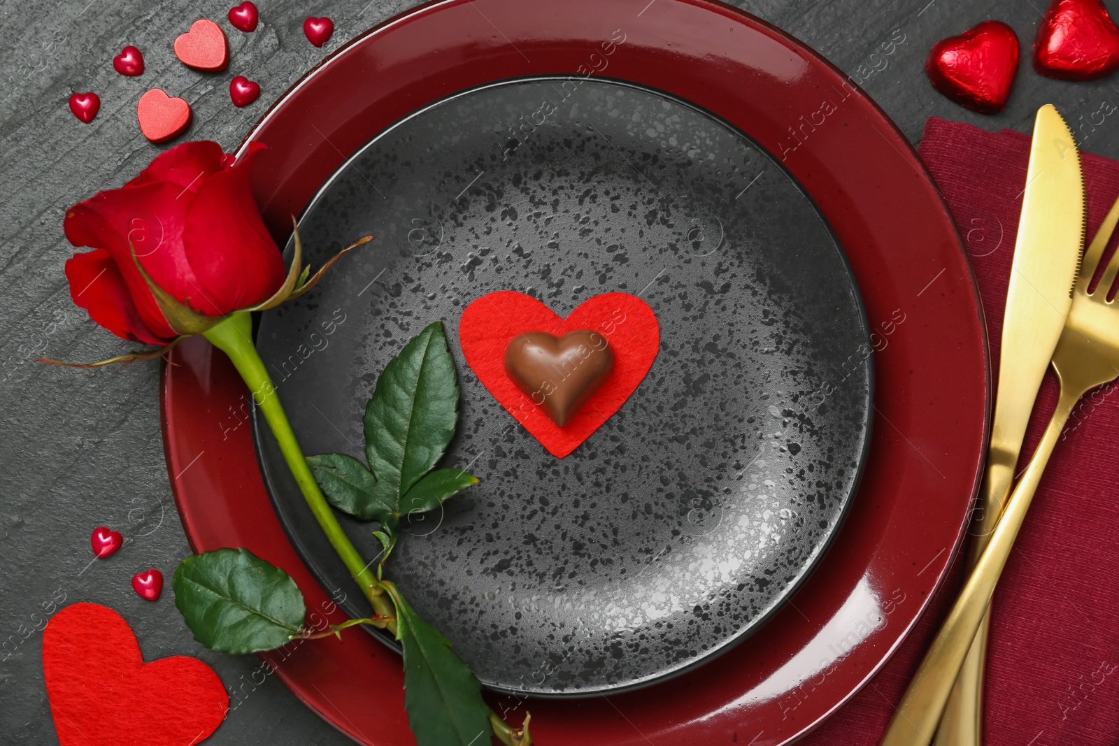 Photo of Romantic place setting with rose and plates on black table, top view. Valentine's day celebration