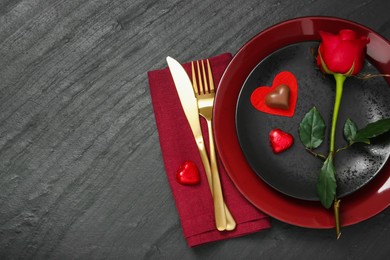 Romantic place setting with rose and plates on black table, top view. Valentine's day celebration