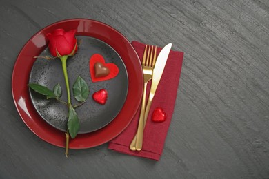 Photo of Romantic place setting with rose and plates on black table, top view. Valentine's day celebration