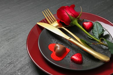 Romantic place setting with rose and plates on black table, closeup. Valentine's day celebration