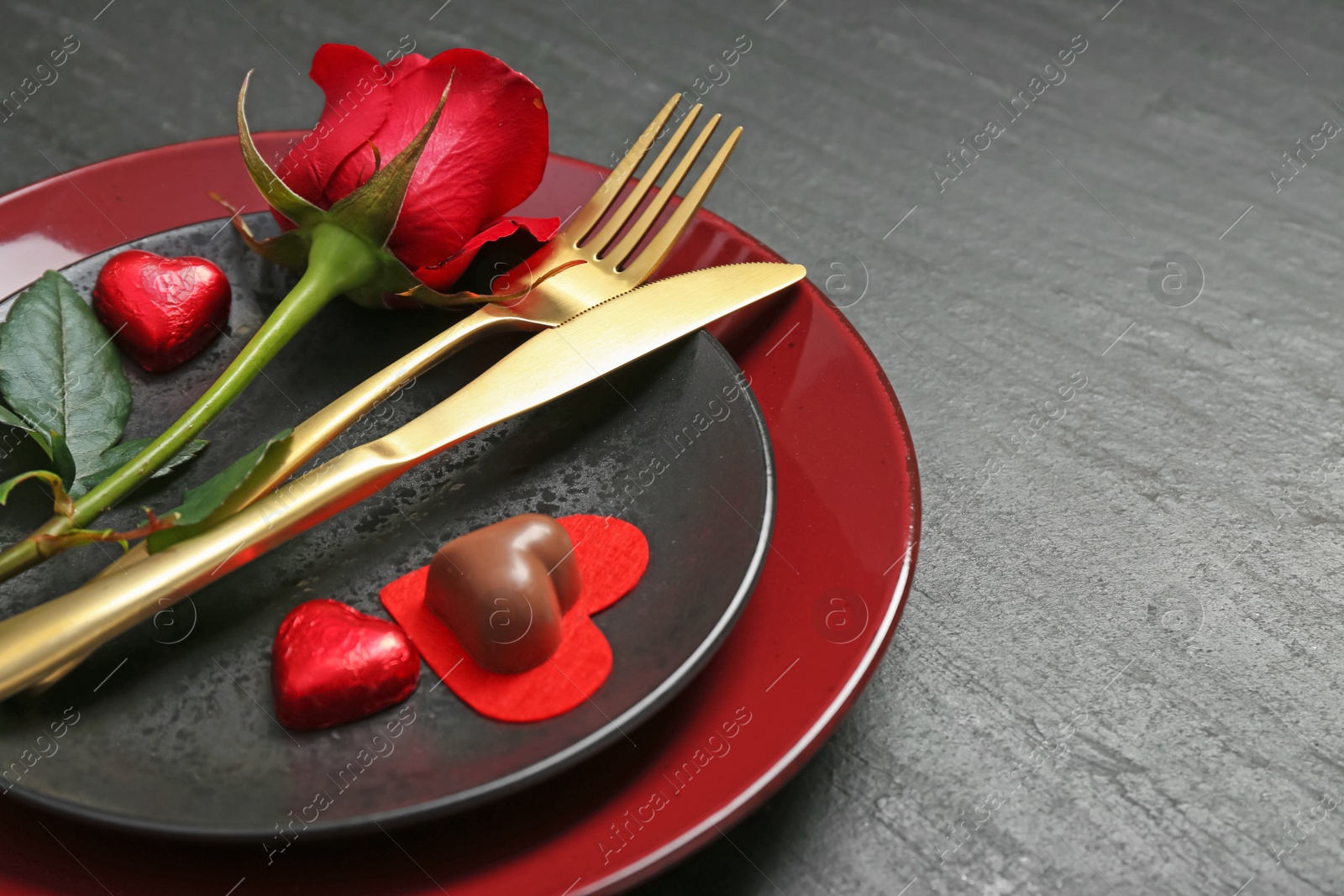 Photo of Romantic place setting with rose and plates on black table, closeup. Valentine's day celebration