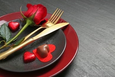 Romantic place setting with rose and plates on black table, closeup. Valentine's day celebration