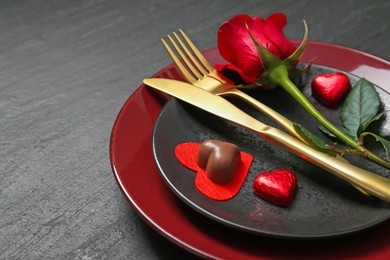 Romantic place setting with rose and plates on black table, closeup. Valentine's day celebration