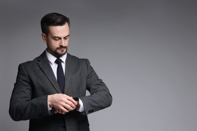 Photo of Confident man in classic suit checking time on grey background. Space for text