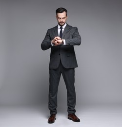 Photo of Confident man in classic suit checking time on grey background