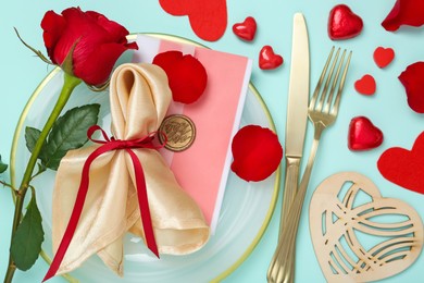 Photo of Romantic place setting with cutlery, hearts and red rose on light blue background, flat lay. Valentine's day celebration