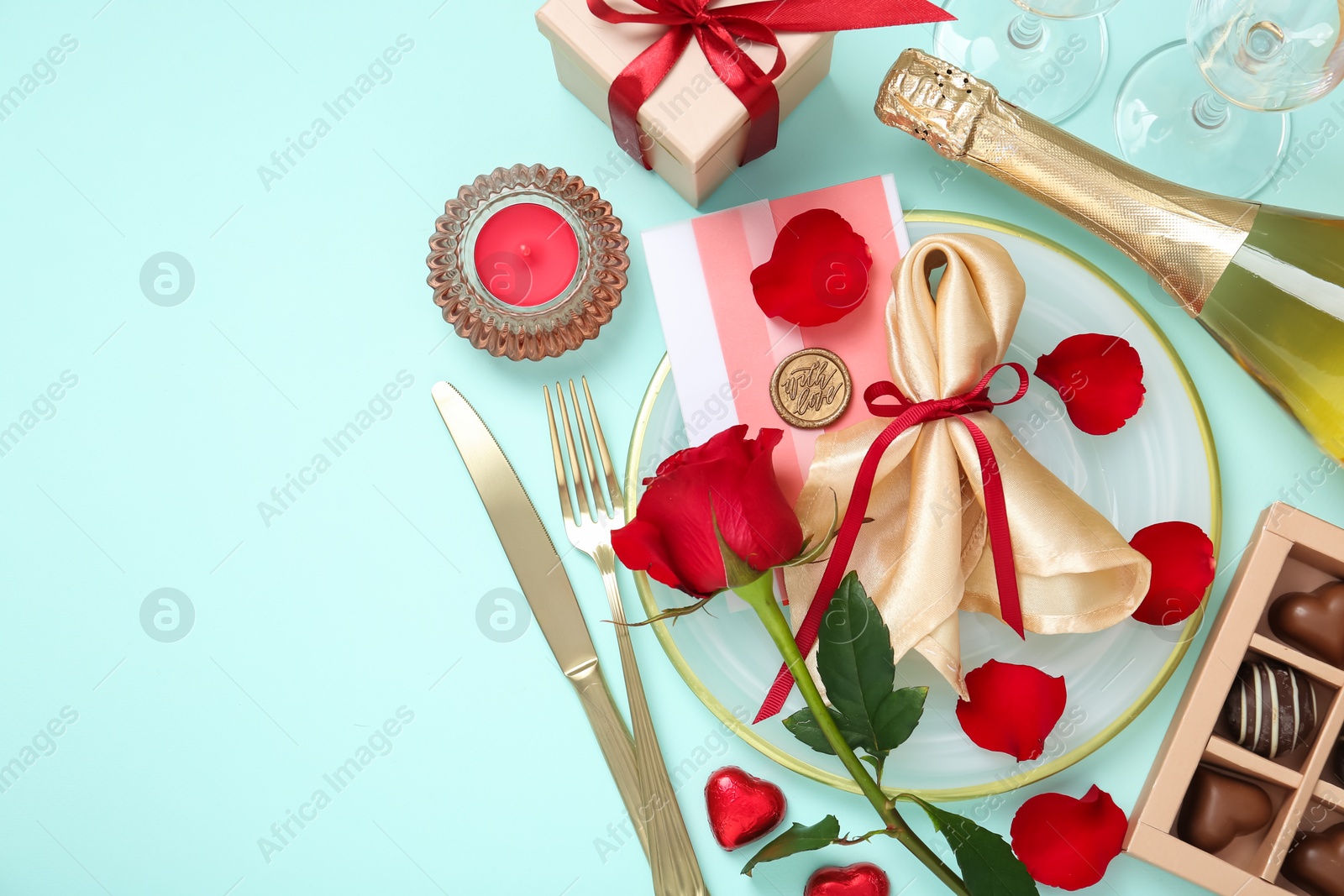 Photo of Valentine's day celebration. Romantic place setting with cutlery, hearts, bottle of champagne and rose on light blue background, flat lay. Space for text