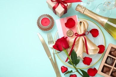 Valentine's day celebration. Romantic place setting with cutlery, hearts, bottle of champagne and rose on light blue background, flat lay. Space for text