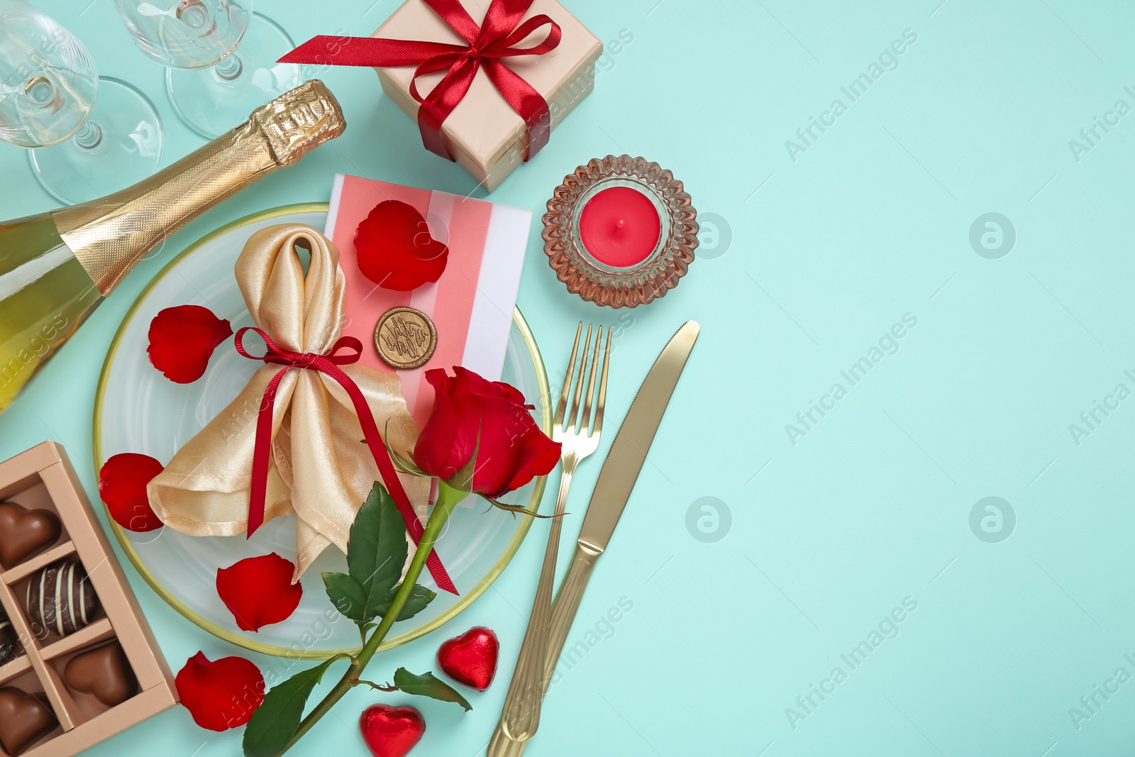 Photo of Valentine's day celebration. Romantic place setting with cutlery, hearts, champagne and rose on light blue background, flat lay. Space for text