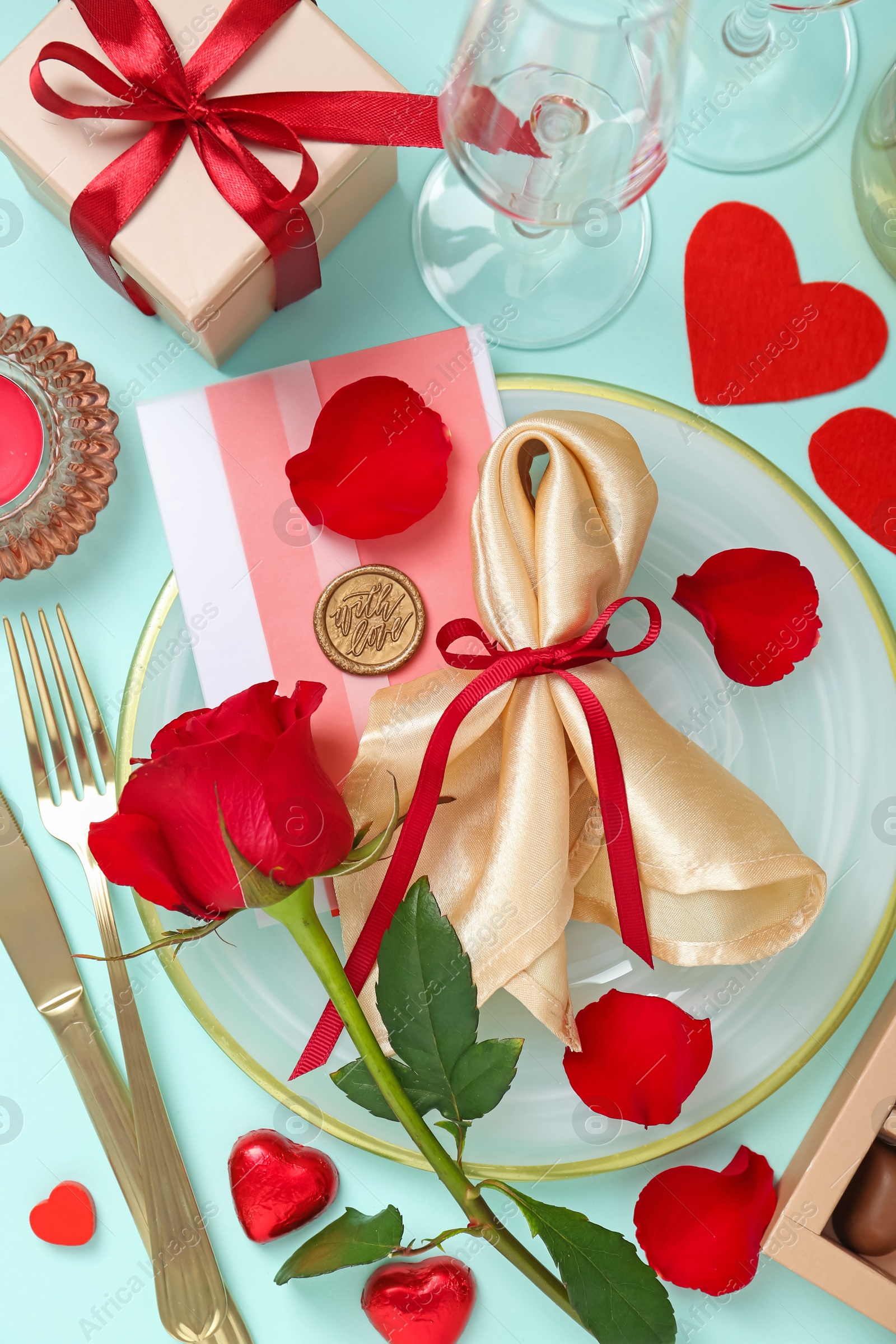 Photo of Romantic place setting with cutlery, hearts, glasses and red rose on light blue background, flat lay. Valentine's day celebration