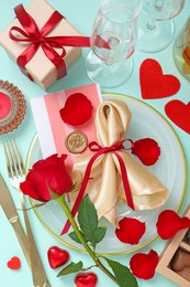 Photo of Romantic place setting with cutlery, hearts, glasses and red rose on light blue background, flat lay. Valentine's day celebration