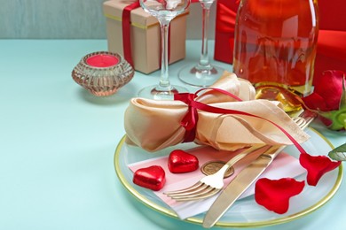 Photo of Valentine's day celebration. Romantic place setting with cutlery, hearts and red rose on light blue table, closeup. Space for text