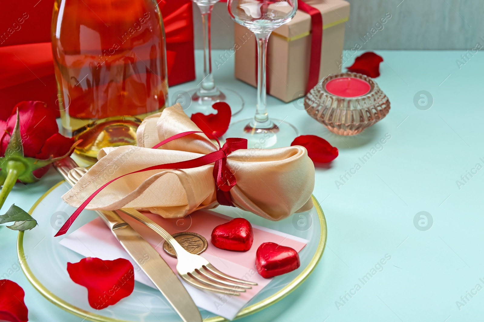 Photo of Valentine's day celebration. Romantic place setting with cutlery, hearts and red rose on light blue table, closeup. Space for text