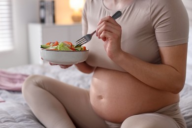 Photo of Pregnant woman eating vegetable salad on bed at home, closeup