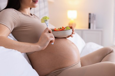 Photo of Pregnant woman eating vegetable salad on bed at home, closeup