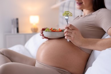 Photo of Pregnant woman eating vegetable salad on bed at home, closeup