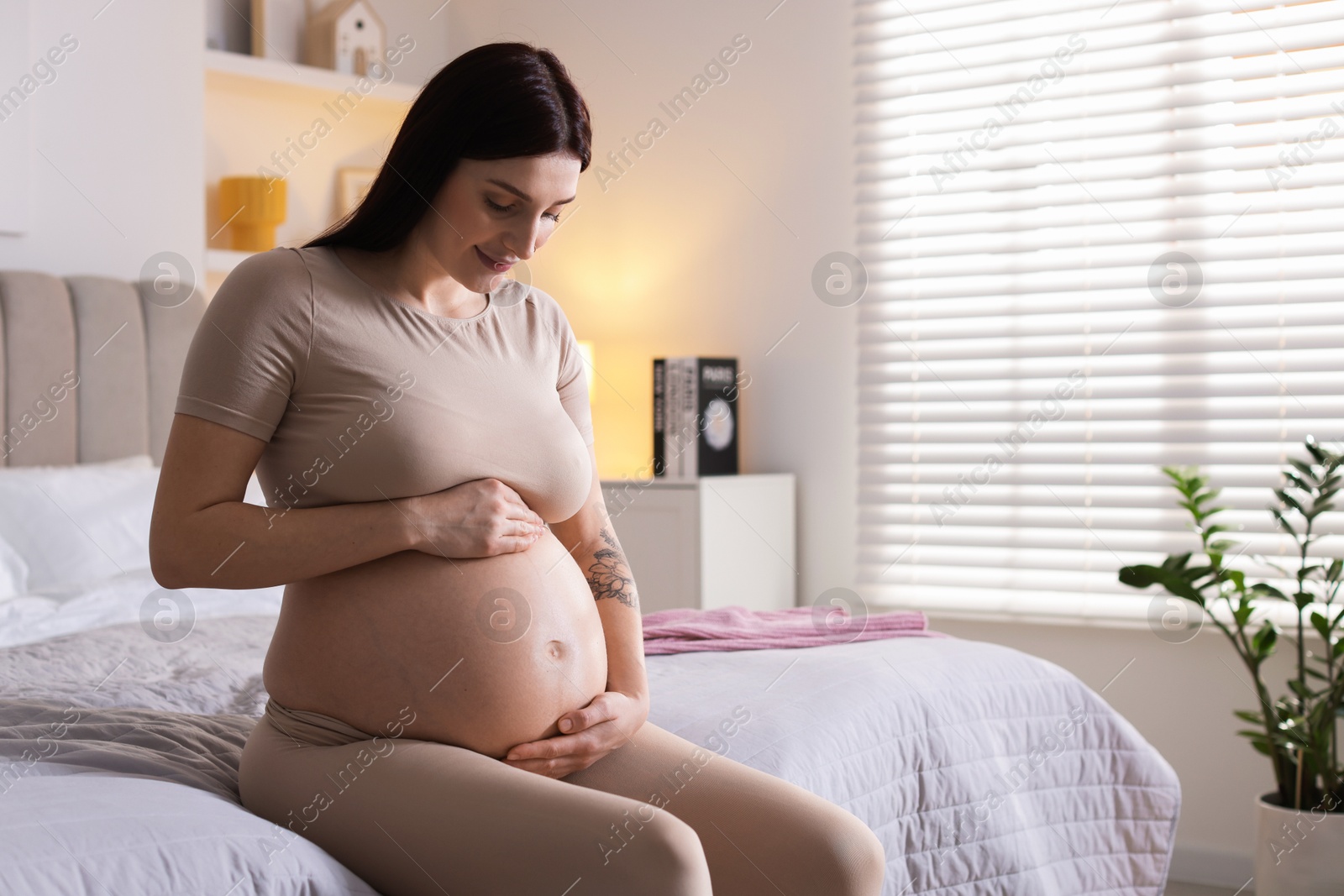 Photo of Beautiful pregnant woman with cute belly on bed at home, space for text