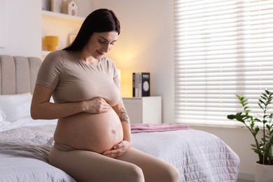 Beautiful pregnant woman with cute belly on bed at home, space for text