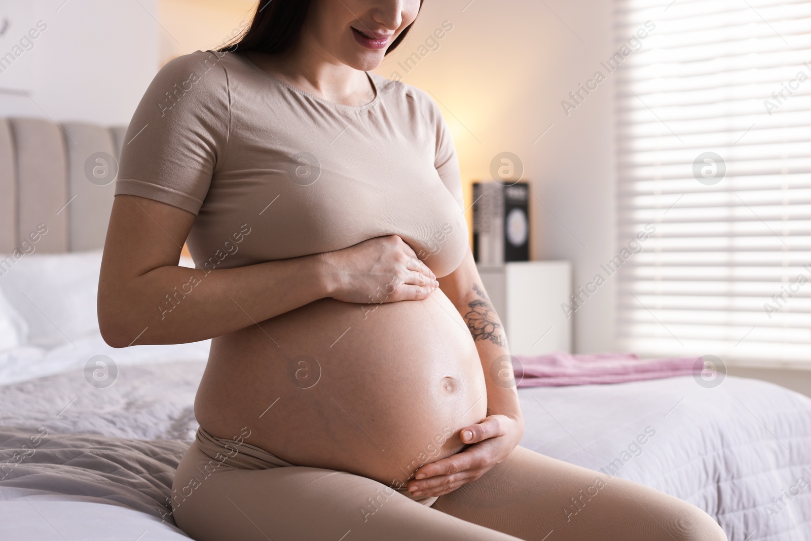 Photo of Pregnant woman with cute belly on bed at home, closeup