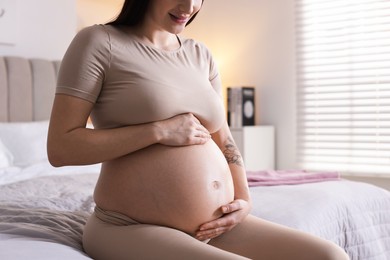 Pregnant woman with cute belly on bed at home, closeup