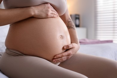 Photo of Pregnant woman with cute belly on bed at home, closeup