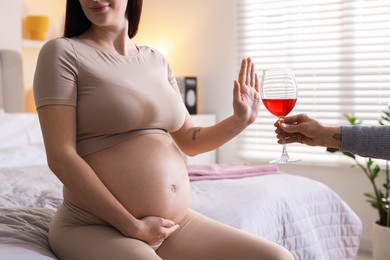 Photo of Pregnant woman refusing glass of red wine at home, closeup